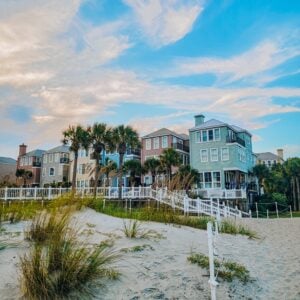 Row of pastel beach houses with palm trees along a sandy coastal area and white fences under a blue sky